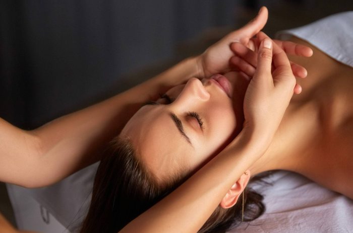Close-up of female enjoying relaxing head and face massage made by masseuse with forearms and cubits in cosmetology spa centre. Body care, skin care, wellness, wellbeing, beauty treatment concept.