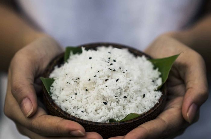 High angle close up of hand holding coconut flesh and black sesame seeds used as a body scrub.